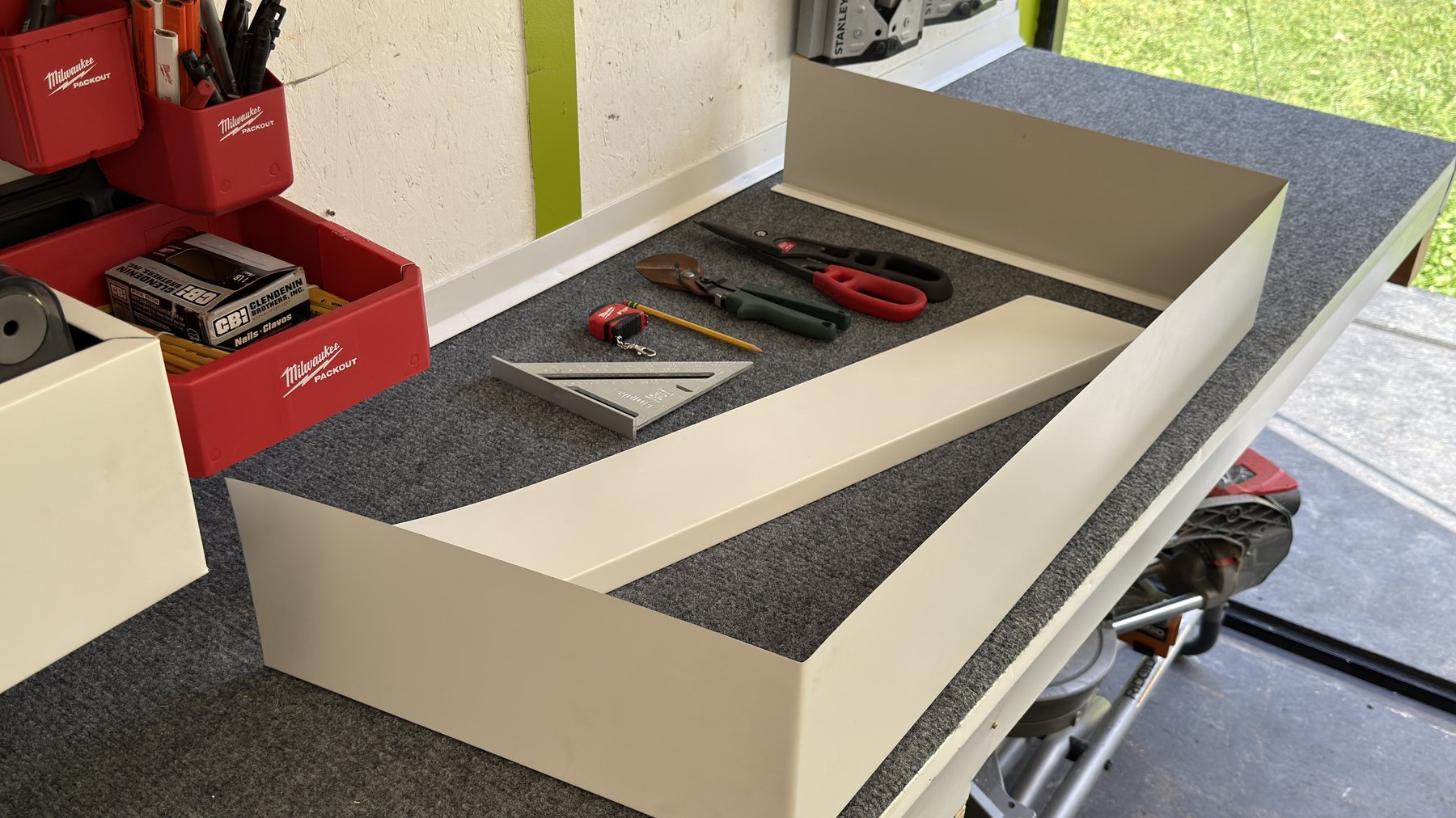 Workbench with freshly bent white aluminum pieces, snips, speed square and pencil